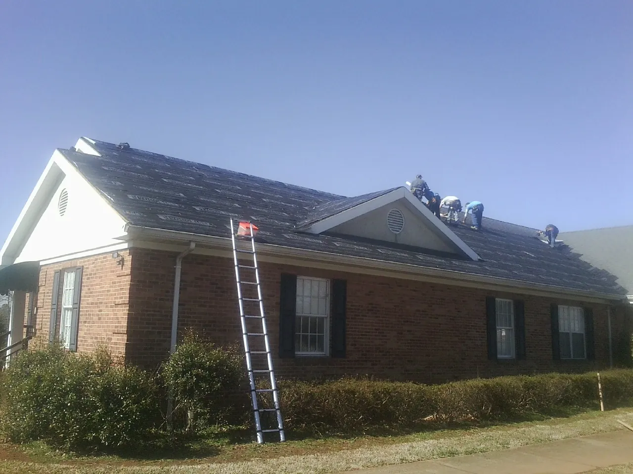 Crew tearing shingles off a brick ranch roof with a ladder set — Metal Roof Repair work by our crew in Redding